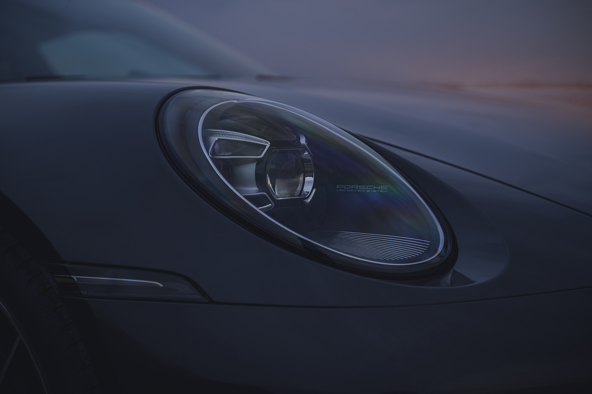 Close-up of Porsche 911 front headlight with LED technology and refined lens design in low-light conditions