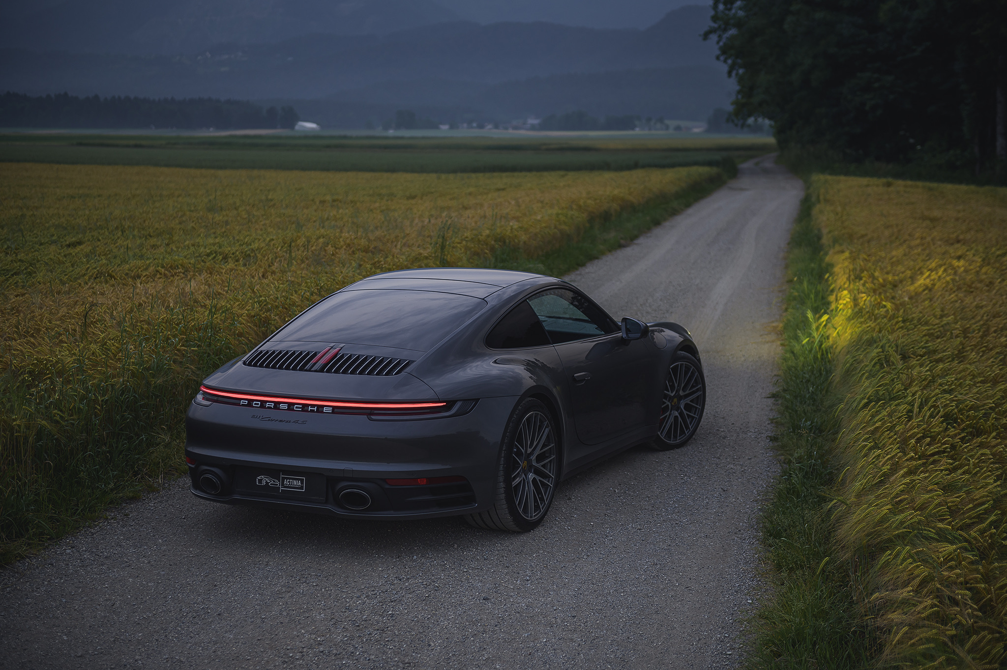Rear view of Porsche 911 driving along a rural road through fields, highlighting sleek design and continuous LED light bar