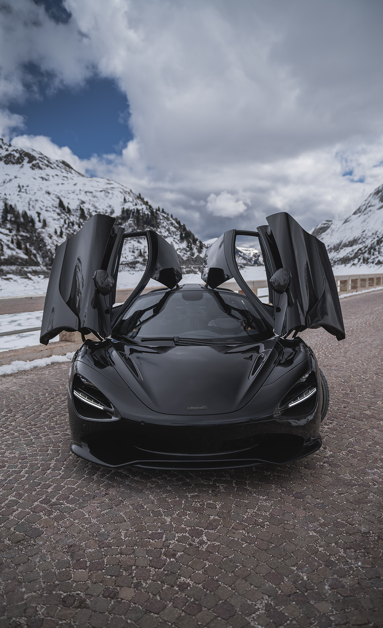 Black McLaren 750S with dihedral doors open at a snowy mountain pass 