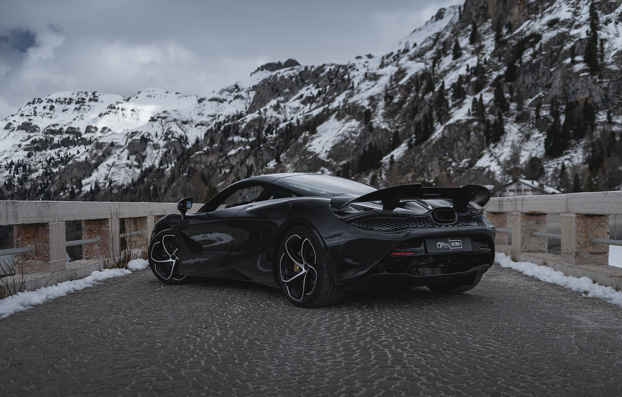 Black McLaren 750S rear view parked at snowy mountain pass in the Alps