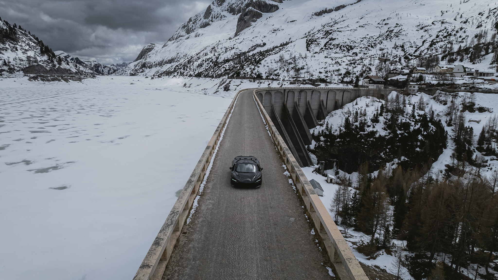 McLaren 750S driving on a dam road through snowy mountains, aerial view